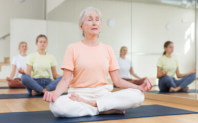 Closeup of positive elderly woman practice yoga lotus pose to meditation in modern studio