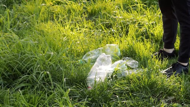 Plastic bottles are thrown on the grass by a person wearing black pants and shoes, highlighting environmental pollution and irresponsible waste disposal