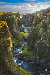 A breathtaking view of Fja&eth;r&aacute;rglj&uacute;fur Canyon with a winding river, moss-covered cliffs, and vibrant vegetation.
