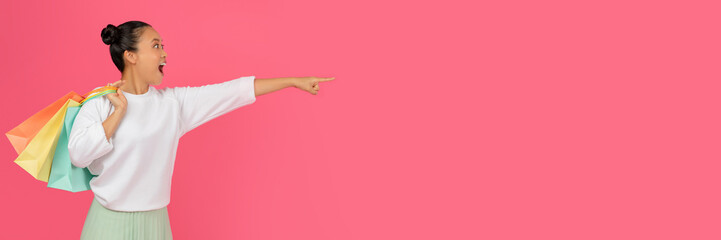 Check This. Amazed Asian Lady Holding Shopping Bags And Pointing Aside At Copy Space, Excited Young Korean Shopaholic Lady Demonstrating Free Place For Advertisement, Standing On Pink Background
