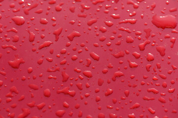 Vibrant droplets of water glisten on a smooth red surface after an evening rain shower