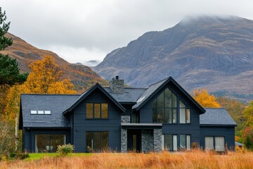 Fototapeta premium Modern black house nestled in the scenic highlands with mountains and autumn foliage in the background under a cloudy sky