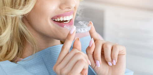 Banner for invisalign orthodontics, modern dentistry concept. Unrecognizable blonde woman with healthy white teeth holding invisible braces while sitting at dental chair, closeup portrait, copy space