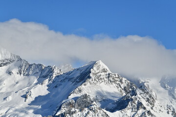 French alps on a sunny day under the clouds by winter covered with snow