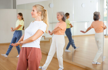 Naklejka premium Middle aged adult athletic blonde woman dancing during group class in dance center