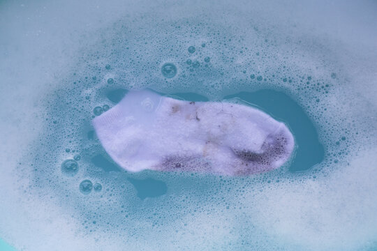 Dirty socks soaked in water, dissolving detergent in blue basin.