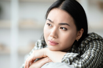 Closeup of upset young woman sitting on couch and crying, living room interior, looking at copy space. Depressed brunette lady suffering from loneliness, staying alone at home, broke up with boyfriend