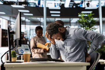 Black enterprise worker takes a break and stretches his back muscles, dealing with a spinal spasm...