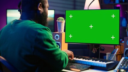 Musician operates on midi controller piano keys next to mockup screen, producing new songs with...