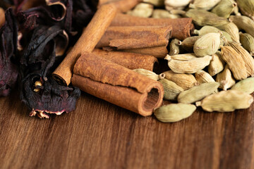 A close-up of aromatic spices featuring dried hibiscus, cinnamon sticks, and green cardamom pods, displayed on a wooden surface.