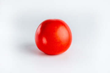 A vibrant red tomato sits against a minimalist white background, showcasing its smooth surface and natural shine.