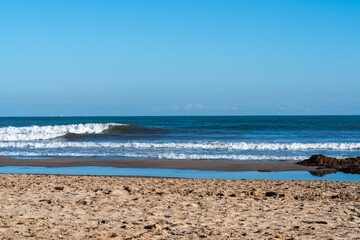 A serene beach scene with gentle waves lapping at the shore, golden sand stretching under a clear blue sky, inviting relaxation and tranquility.