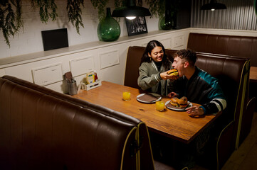 Young woman feeding a burger to her boyfriend while having dinner in a vintage restaurant