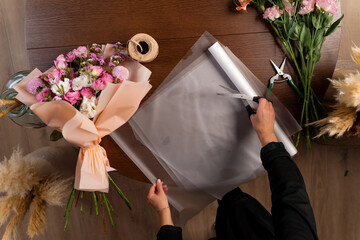 Wrapping bouquets of flowers into craft paper by florist. Collecting compositions of bloom mixed...
