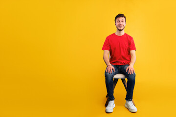 Fototapeta premium Casually Handsome. Studio shot of young man sitting on the chair and looking aside at copy space, blue wall