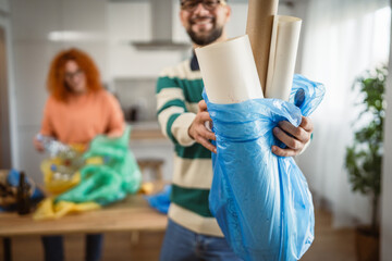 man throwing paper in blue garbage bag at home