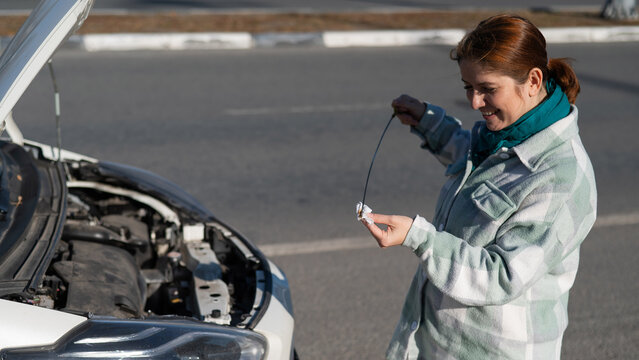 Caucasian female driver checking oil level in car engine. 