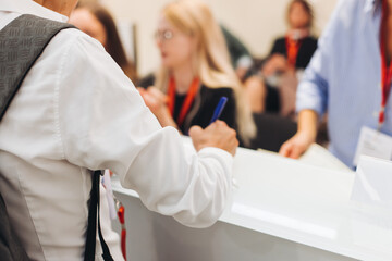 Process of checking in on conference congress forum event, registration desk table, visitors and attendees receiving lanyard with name badge and entry wristband bracelet and register electronic ticket