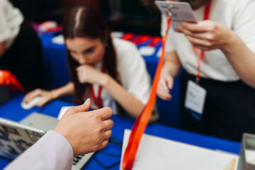Process of checking in on conference congress forum event, registration desk table, visitors and attendees receiving lanyard with name badge and entry wristband bracelet and register electronic ticket
