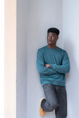 Young man with arms crossed leaning against wall looking away