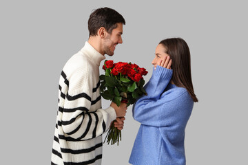 Beautiful young couple with bouquet of red roses on grey background. Valentine's day celebration