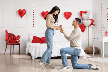 Young man proposing to his girlfriend in bedroom. Valentine's Day celebration