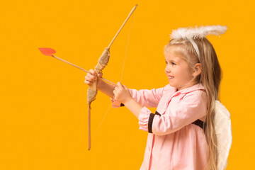 Cute little girl dressed as cupid with bow and arrow on yellow background. Valentine's Day...