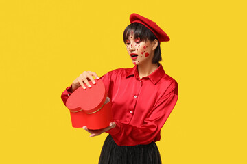 Beautiful young woman with creative makeup opening heart-shaped gift box for Valentines Day on yellow background