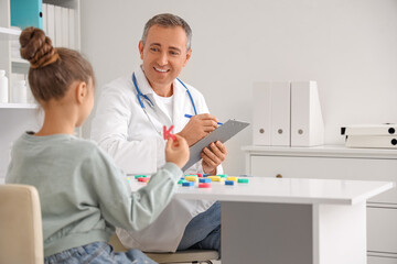 Obraz premium Male speech therapist working with little girl at table in clinic
