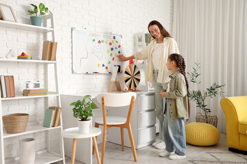 Female speech therapist working with little girl near whiteboard in office