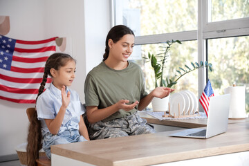Female soldier with her daughter video chatting in kitchen