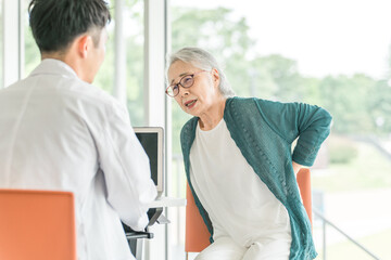 病院で腰の痛みを相談するシニア女性と診察する若い男性医師
