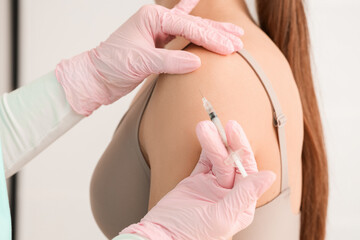 Fototapeta premium Young woman receiving injection in her shoulder at cosmetologist's office, closeup