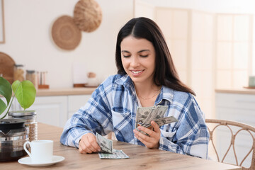 Beautiful woman counting dollar banknotes at table in kitchen