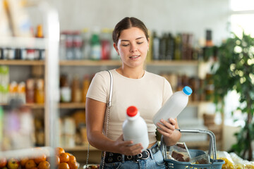 Young woman buyer chooses milk in bottle in grocery store