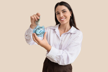 Beautiful woman putting money into piggy bank on beige background