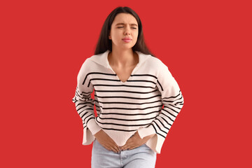 Young woman suffering from menstrual cramps on red background