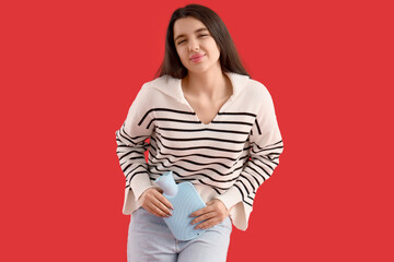 Young woman with hot water bottle suffering from menstrual cramps on red background