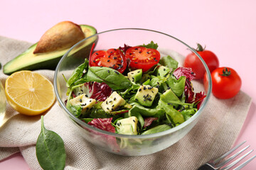 Glass bowl of tasty avocado salad with cherry tomatoes and lemon on pink background