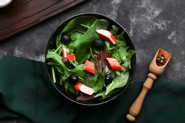 Bowl of salad with crab sticks, spinach, cucumber and wooden scoop on black grunge background © Pixel-Shot
