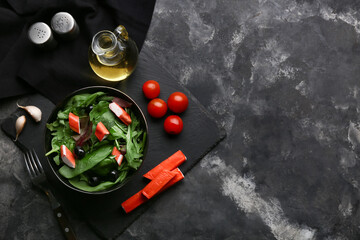 Plate of salad with crab sticks, spinach, black olives and ingredients on grey grunge background