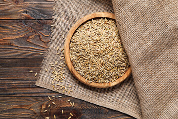 Plate with oat seeds and burlap fabric on wooden background