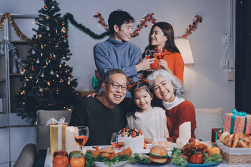 Multi-Generation Family Celebrate Christmas At Home Wearing Santa Hats And Antlers Opening Presents