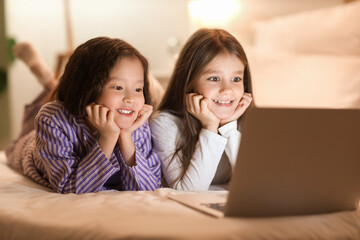 Cute girls watching cartoons on laptop in bedroom at night