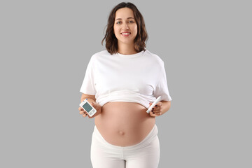 Young pregnant woman with glucometer and lancet pen on light background. Gestational diabetes...