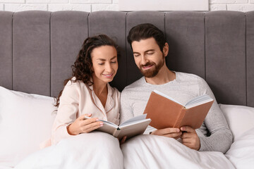 Happy couple reading books under blanket in bedroom
