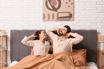 Happy couple in pajamas stretching on bed at home