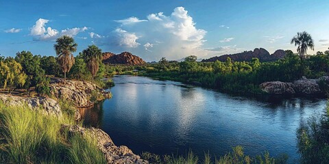 Obraz premium Calm river flows past lush vegetation, red rocks in background, sunset. Nature scene