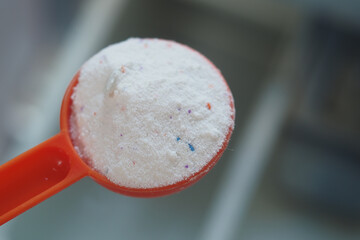 Washing powder in plastic spoon on blue background 