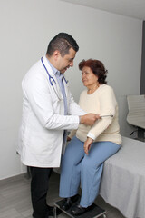 Obraz premium Dark-skinned Latino man medical doctor attends to elderly woman patient performs a reflex check in his office